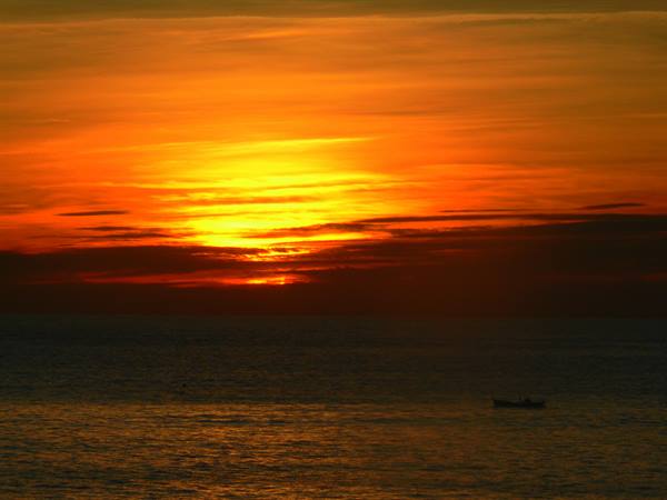 Orange sun low over the sea horizon, small fishing boat in backlight