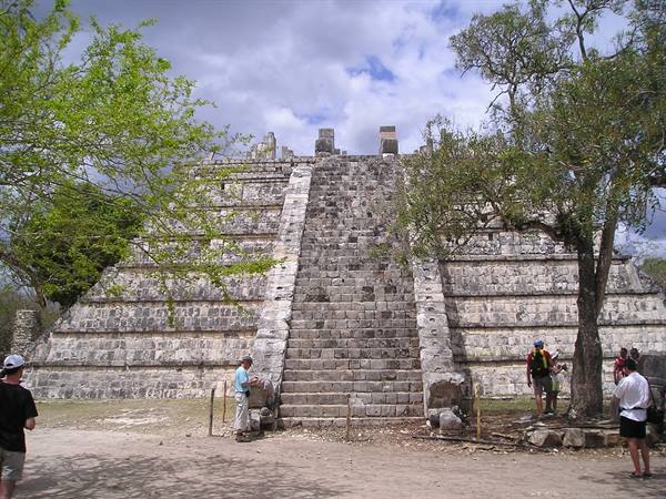 Tourists at the base of the stone pyramid at Chichén Itzá among trees