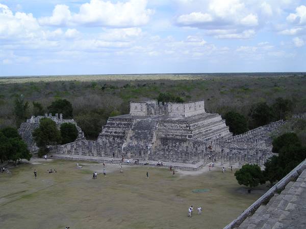 Mayan stone temple at Chichén Itzá, tourists walk across grass under clouds