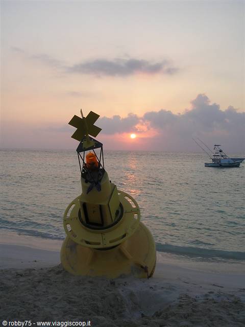Yellow buoy stranded on the beach, boat offshore, low sun among clouds