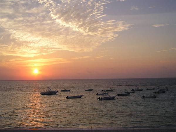 Boats anchored on calm sea under the low sun and golden clouds