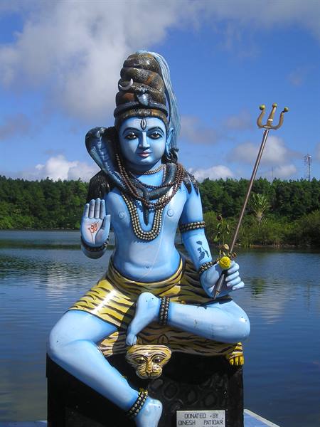 Painted statue of Shiva holding a trident, seated beside a lake