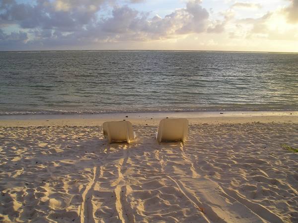Two empty plastic lounge chairs on sand facing the calm sea