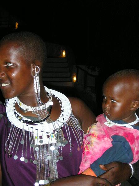 Woman wearing white beaded necklaces holds a child in the night