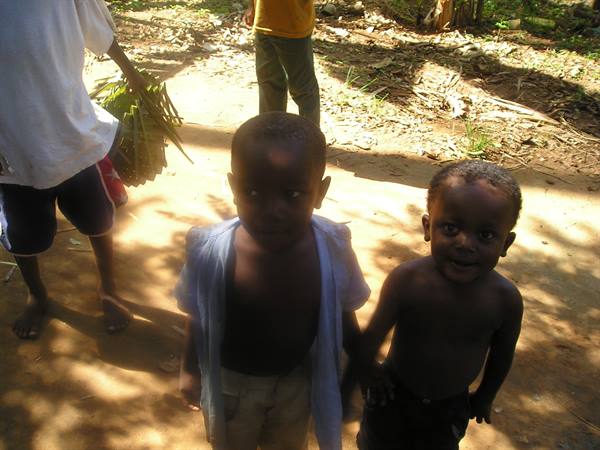 Two African children hold hands on a shaded dirt path