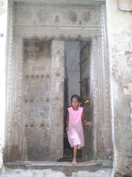Girl in pink on an ornate carved wooden door, Stone Town