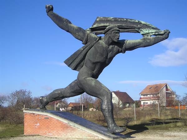 Bronze statue of a striding man with windblown cape on brick base