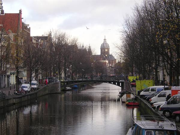 Amsterdam canal with bridge, brick houses and church dome under cloudy sky