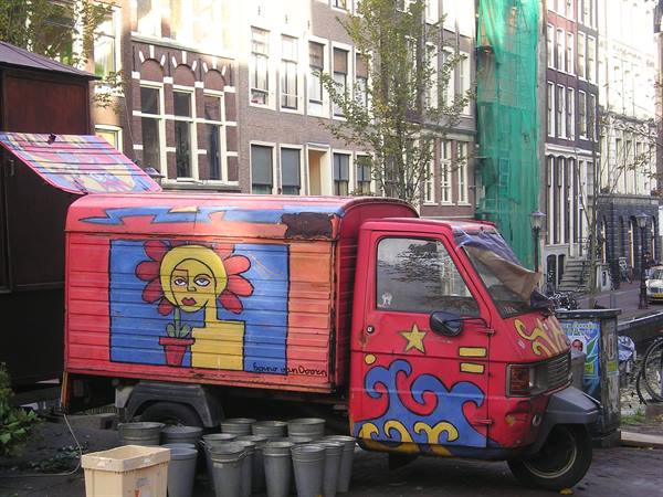 Painted Ape van with colorful flowers beside Amsterdam canal houses