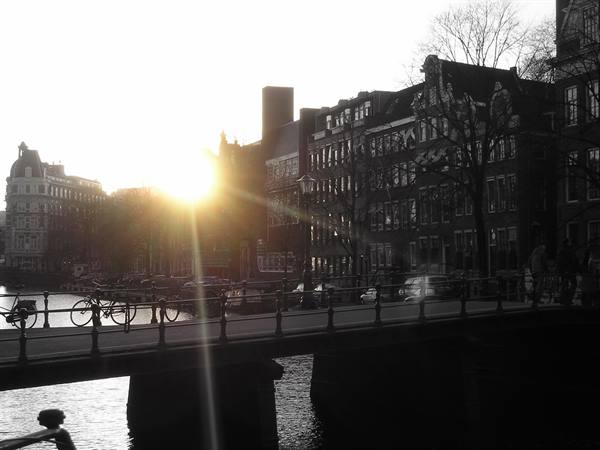 Bicycles on an iron bridge in Amsterdam, canal houses against the low sun