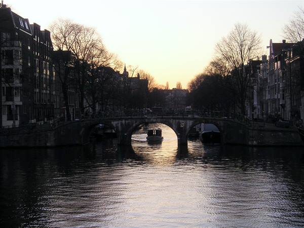 Boat passing under a brick bridge on Amsterdam canals at dawn