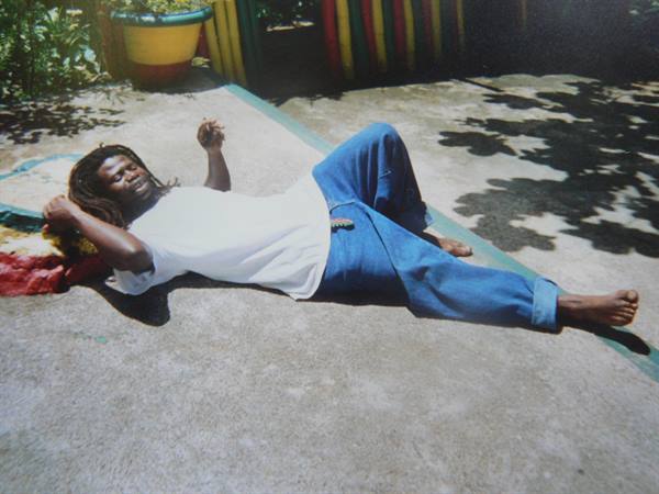 Man with dreadlocks lying on sunlit concrete, white t-shirt and blue jeans
