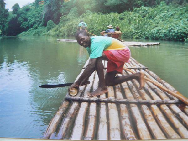 Smiling man stands on a bamboo raft on the river, other rafts behind