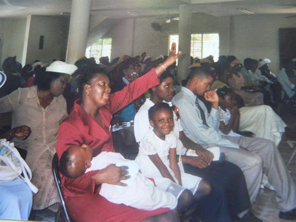 Woman in red raising her arm at church service, holding a baby on her lap