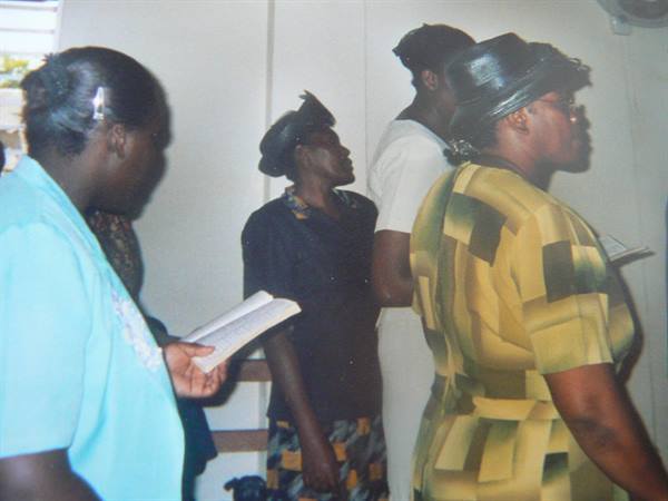 Women wearing hats holding hymn books standing during a church service