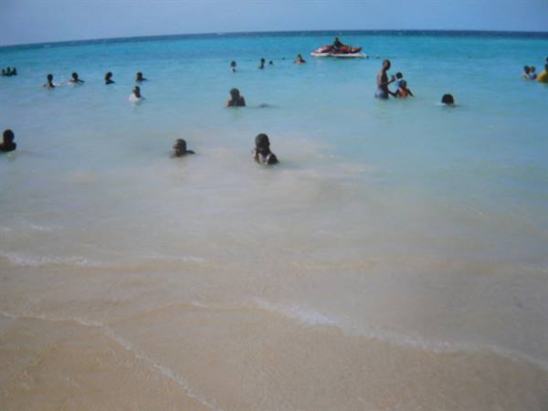 Swimmers in turquoise water off the sandy beach, jet ski in the distance