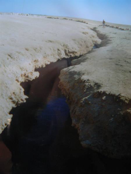 Deep crack in salt crust, a person walks along the edge