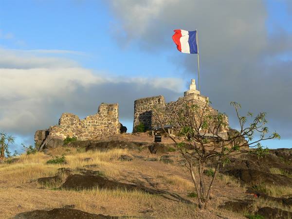 French flag flying over old stone fortress ruins on a grassy hill