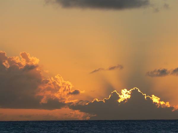 Sun rays breaking behind golden clouds over calm sea