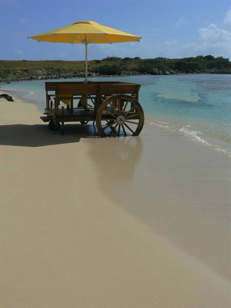Wooden cart with yellow umbrella on the sand beside turquoise water
