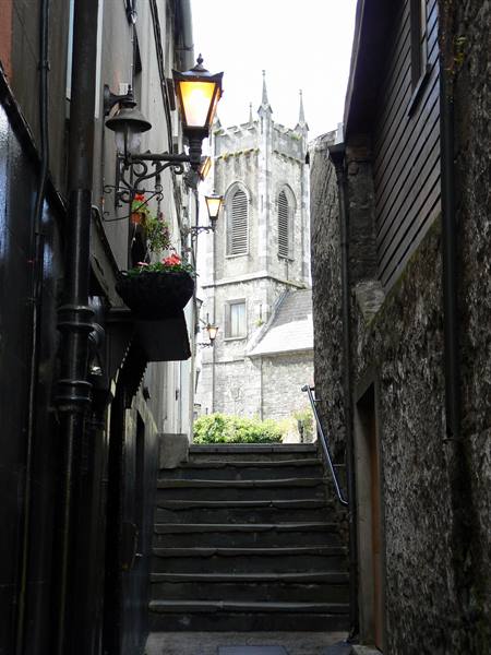 Stone steps between old walls, lit lanterns and Gothic church tower