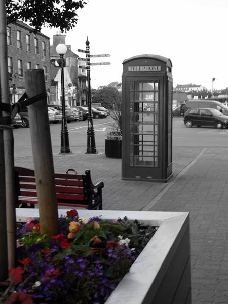 Red telephone box on a town square, wooden bench and colourful flowers