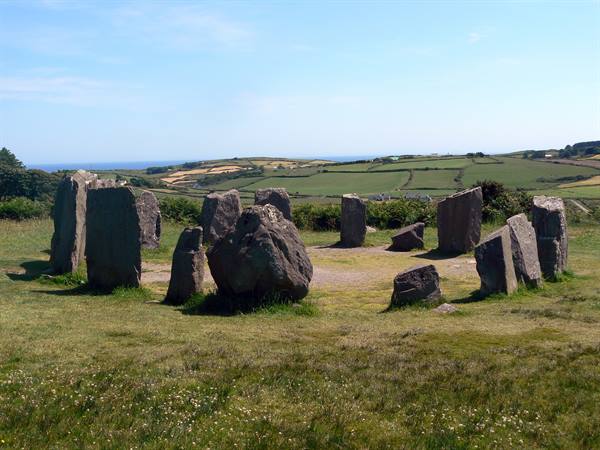 Drombeg stone circle, megaliths standing in a ring on green grass under blue sky