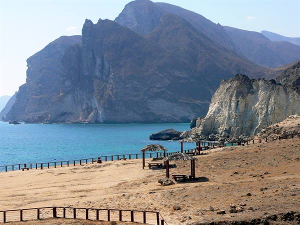 Sandy beach with straw umbrellas, white cliffs and mountains rising above turquoise sea