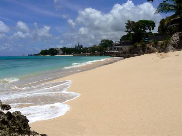 White sand beach with foamy waves, palm trees and resorts under clouds