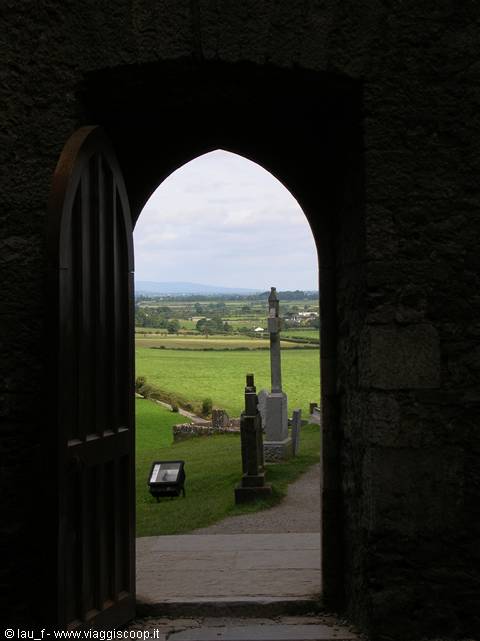 Arched stone doorway opens onto graveyard and green fields at the Rock of Cashel