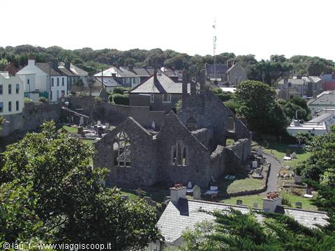 Stone church ruins with graveyard and houses among green trees