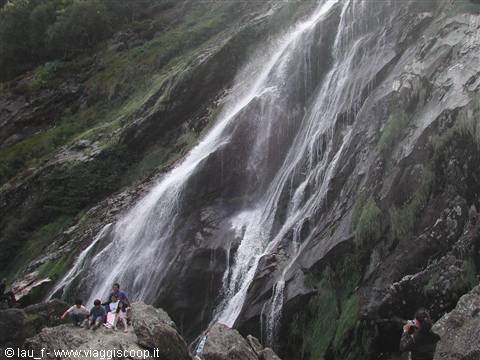 Tourists sitting on boulders at the base of Powerscourt Waterfall among mossy rock