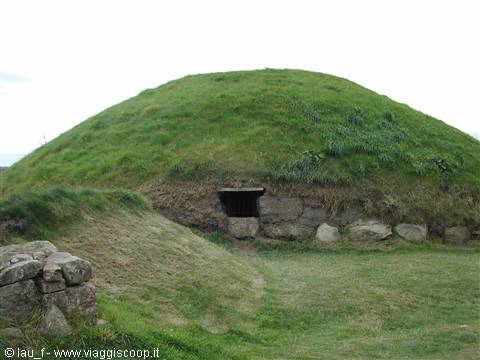 Ancient grass-covered burial mound with stone entrance under pale sky