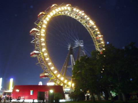 The illuminated Wiener Riesenrad ferris wheel at night among trees