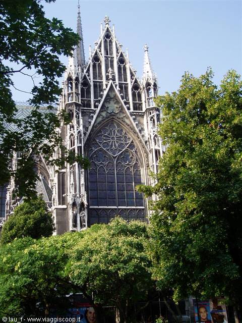 Gothic facade of the Votivkirche among green trees in Vienna