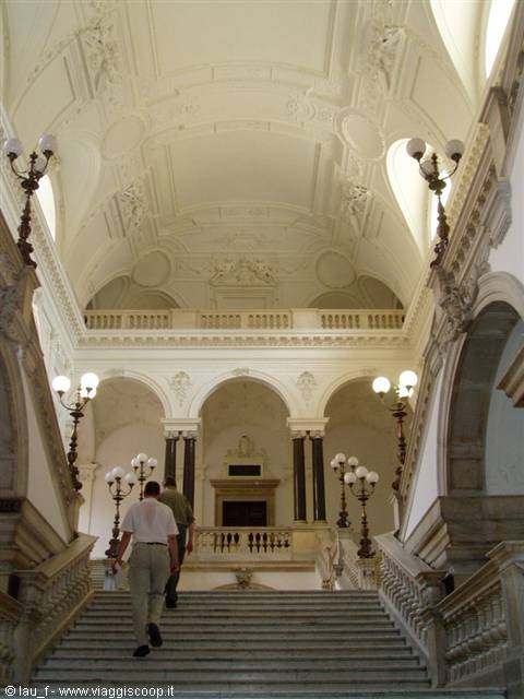 Two visitors climb a marble staircase among lamps and white arches