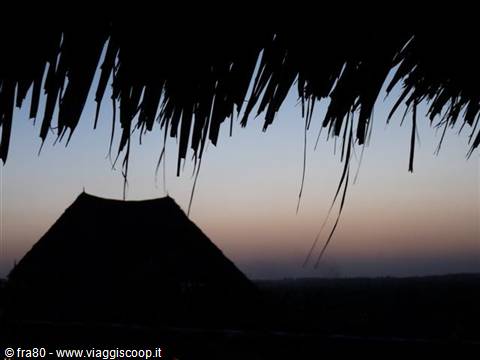 Thatched roof silhouetted at dusk, orange and blue sky above a cone-shaped roof