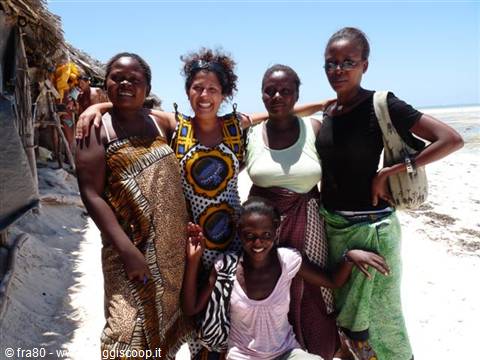 Women and a smiling child pose with a tourist on the white sand beach