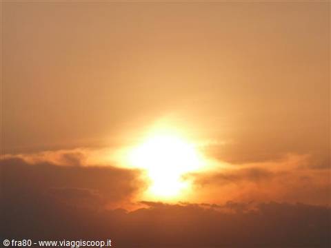 Bright sun glowing through orange clouds in hazy sky