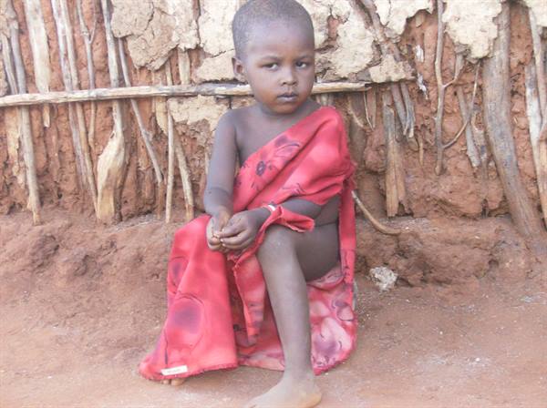 Child wrapped in red cloth sitting before mud and stick wall