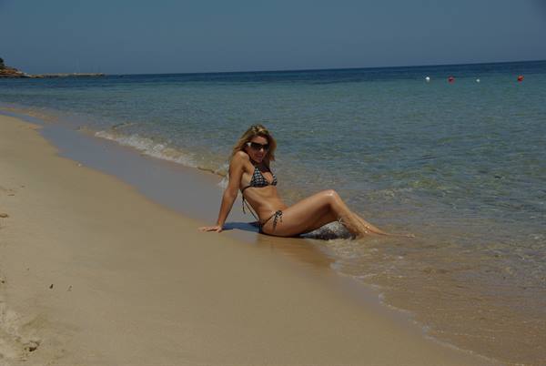 Woman in bikini sitting on wet sand as clear waves wash over her legs