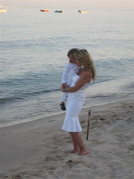 Woman in white dress on the beach, holding a child in her arms