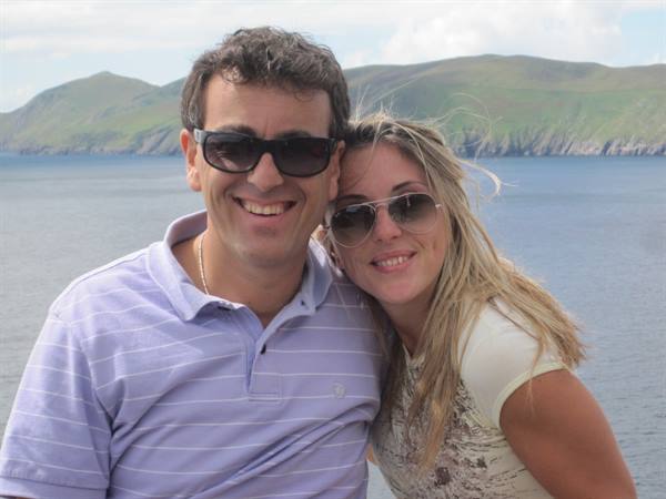 Smiling couple wearing sunglasses by the sea and green hills