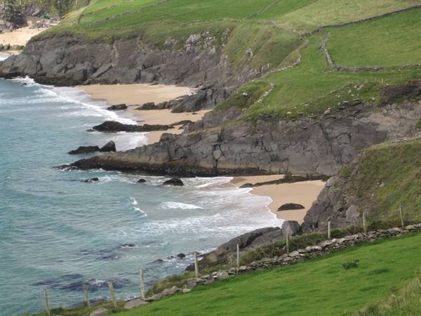Dark cliffs over sandy beaches, green fields with stone walls, turquoise waves