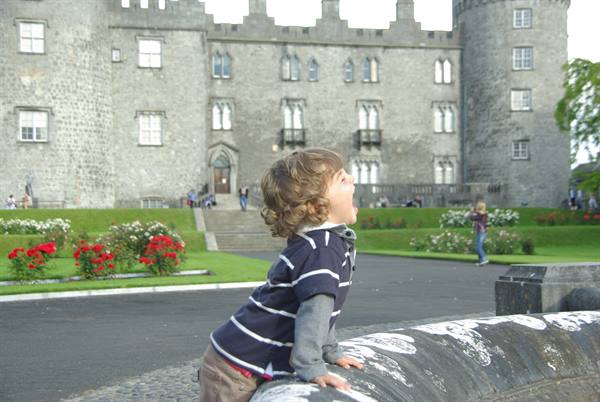 Laughing child leaning on a stone fountain in front of Kilkenny Castle