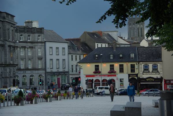 Stone square with pedestrians, flowers, pubs and a cathedral tower among Georgian buildings