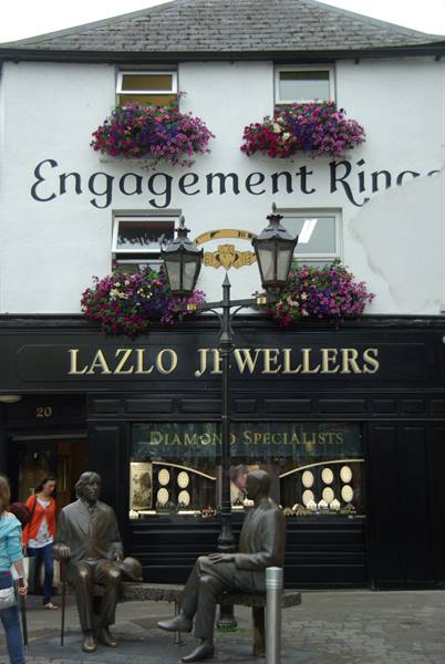 Bronze statues in front of Lazlo Jewellers, Engagement Rings sign and hanging flowers