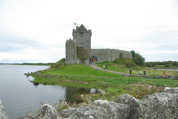Tourists walk up to Dunguaire Castle, stone fortress by the bay