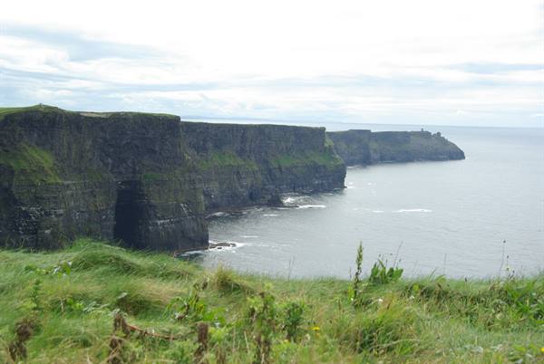Cliffs of Moher, dark rock over the ocean, green grass, cloudy sky