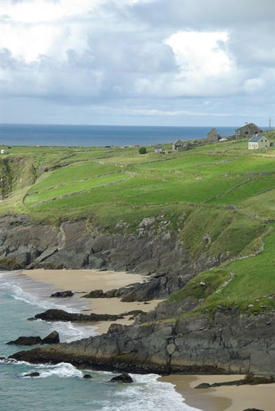 Green cliffs with stone walls, cottages and sandy beach by the ocean